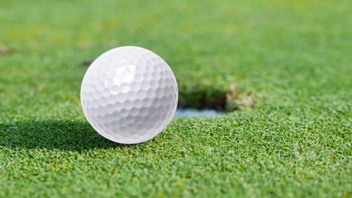 Golfball liegt neben dem Loch auf dem Green