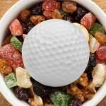 Rundenverpflegung: 10 Leckere Snacks für die Golfrunde Eine Schale mit Nüssen, auf denen ein Golfball liegt