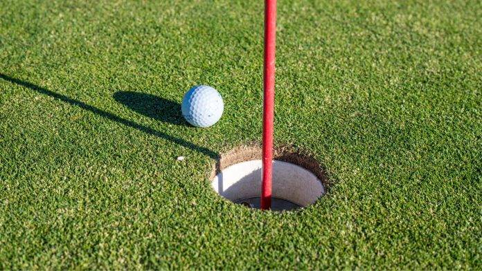 Golfball liegt neben dem Loch auf dem Grün