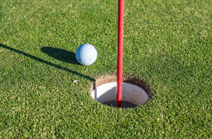Golfball liegt neben dem Loch auf dem Grün